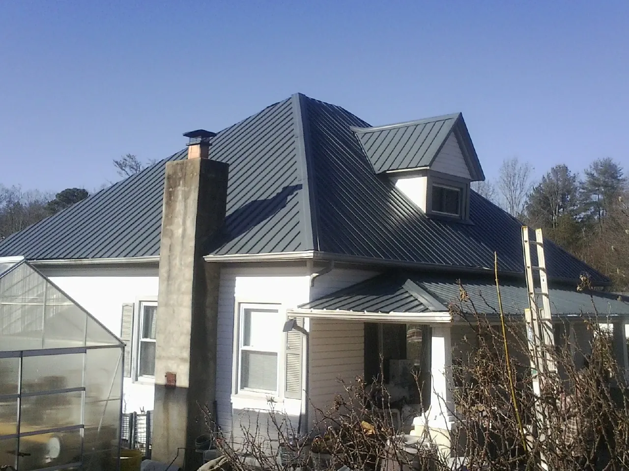 Dark blue standing seam metal roof on a white farmhouse with dormer — Slate & Tile Roof Repair by Roofing Brothers in Beechgrove