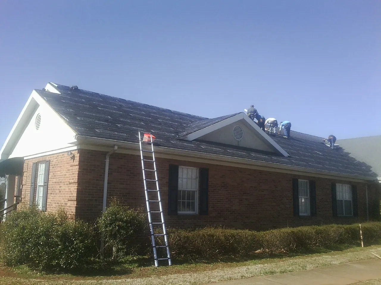 Crew tearing shingles off a brick ranch roof with a ladder set — Metal Roof Repair work by our crew in Beechgrove