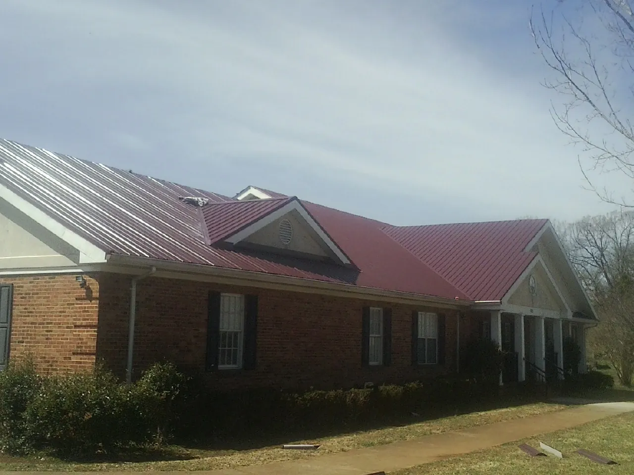 Red metal roof with gabled entries on a long brick building, from a Hail Damage Roof Repair job in Beechgrove