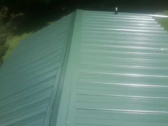 New green metal panels meeting at the ridge of a roof — Flat Roof Repair work by our crew in Beechgrove