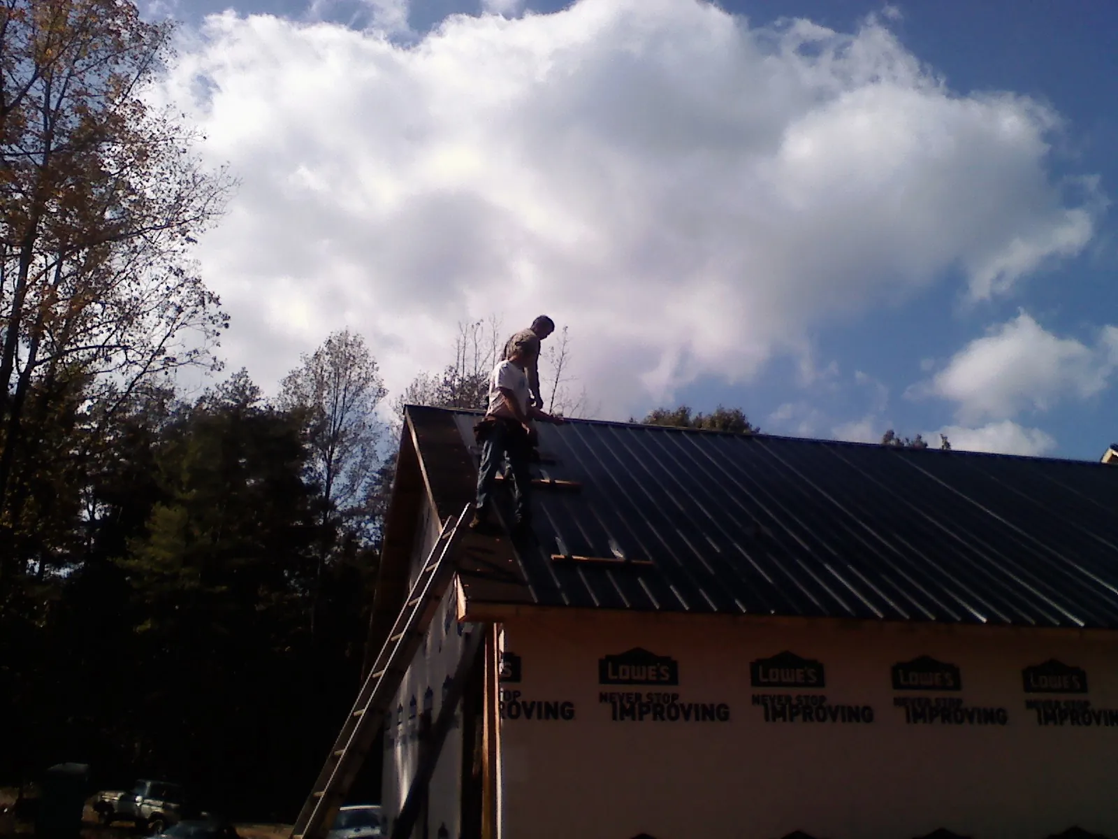 Roofer fastening dark metal panels high against a cloudy sky, from a Roof Inspection job in Beechgrove