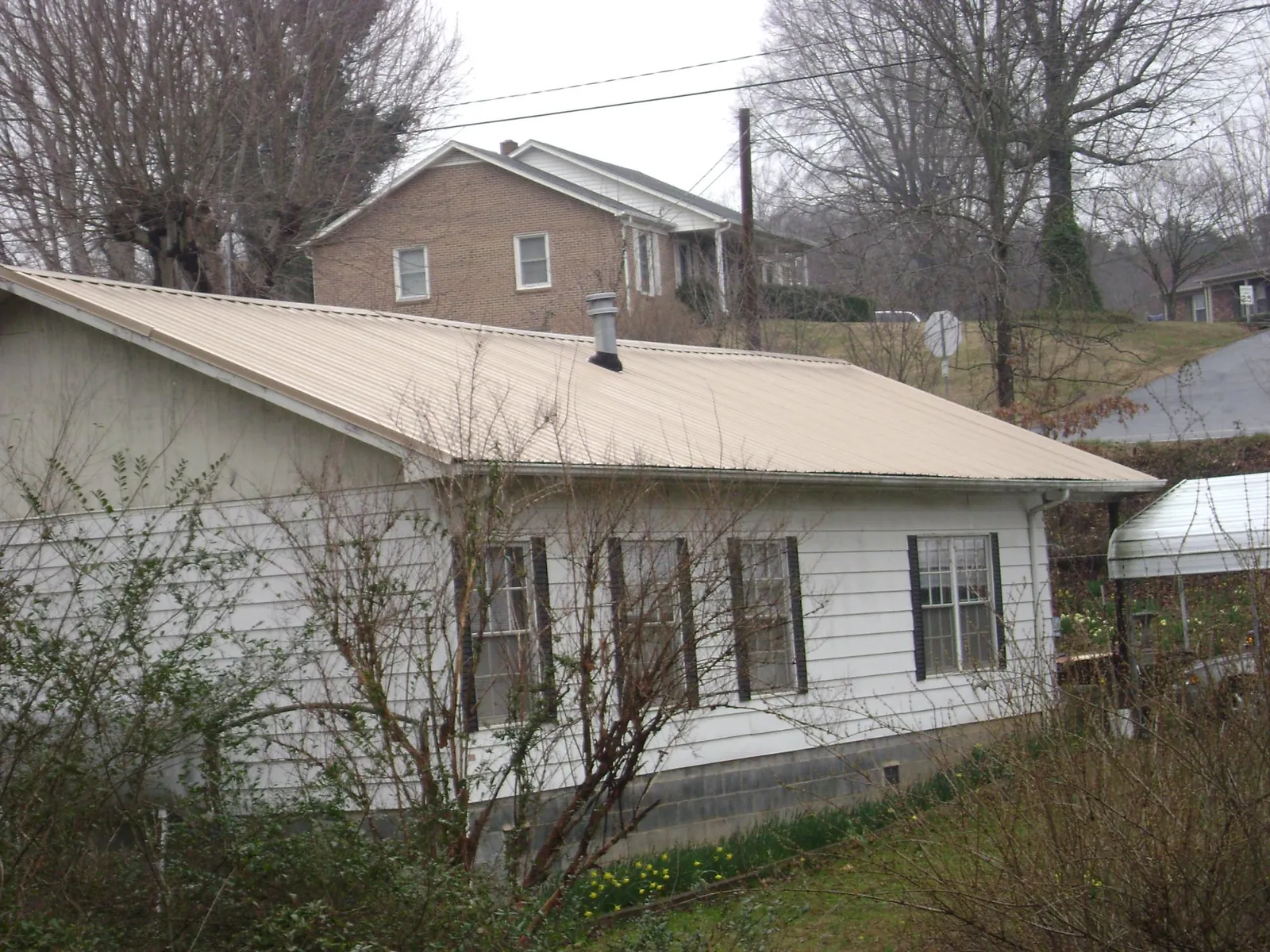 Tan metal roof on a white sided house set into a hillside — Commercial Roofing by Roofing Brothers in Beechgrove