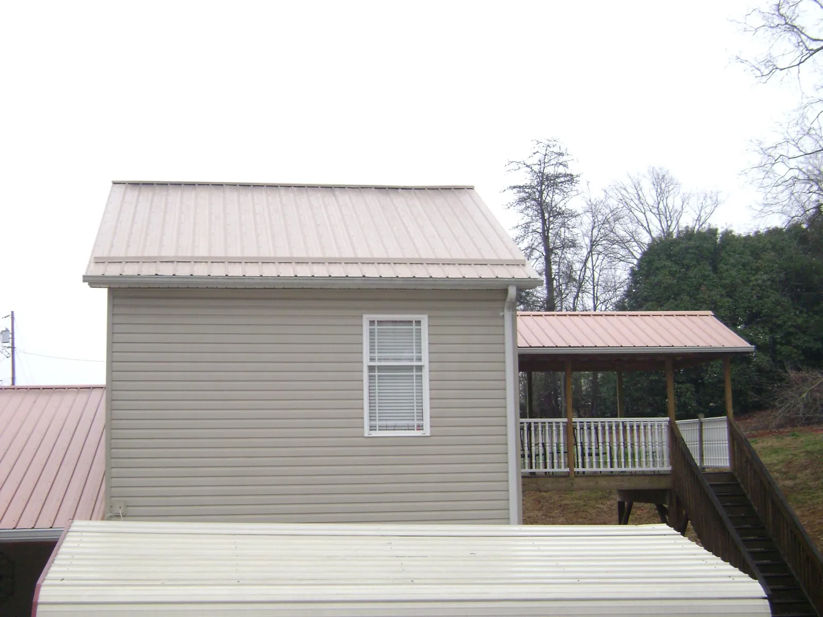 Tan metal roofs on a two story addition and attached porch, from a Roof Replacement job in Beechgrove